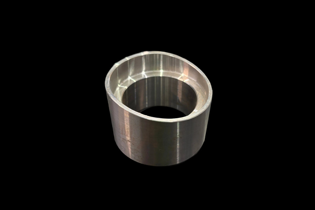 A machined ball joint cup or bushing with a polished inner surface, resting on a dark wood-grained tabletop.