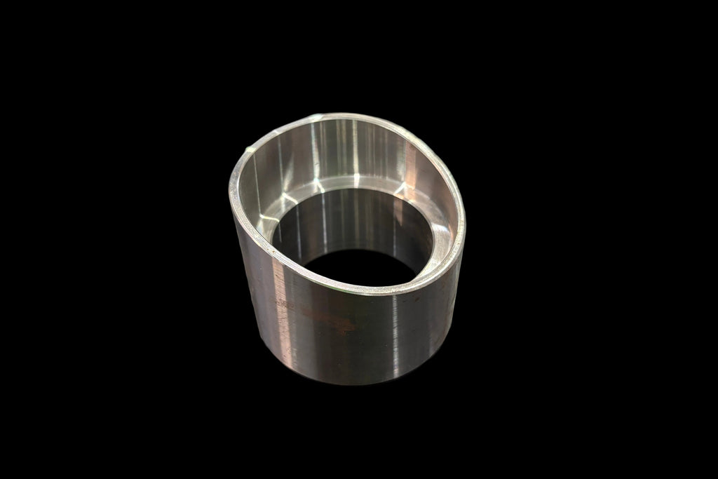 A machined ball joint cup or bushing with a polished silver finish, standing on a dark wood-grained tabletop.