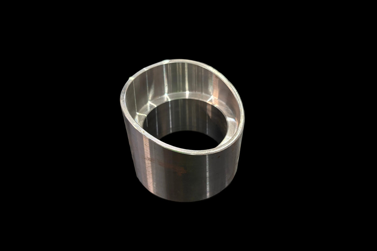 A machined ball joint cup or bushing with a polished silver finish, standing on a dark wood-grained tabletop.