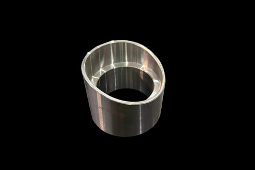 A machined ball joint cup or bushing with a polished silver finish, standing on a dark wood-grained tabletop.